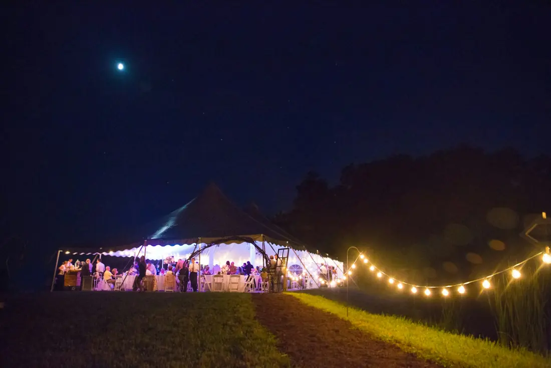 Lit wedding marquee on a lawn at night by Events by OT